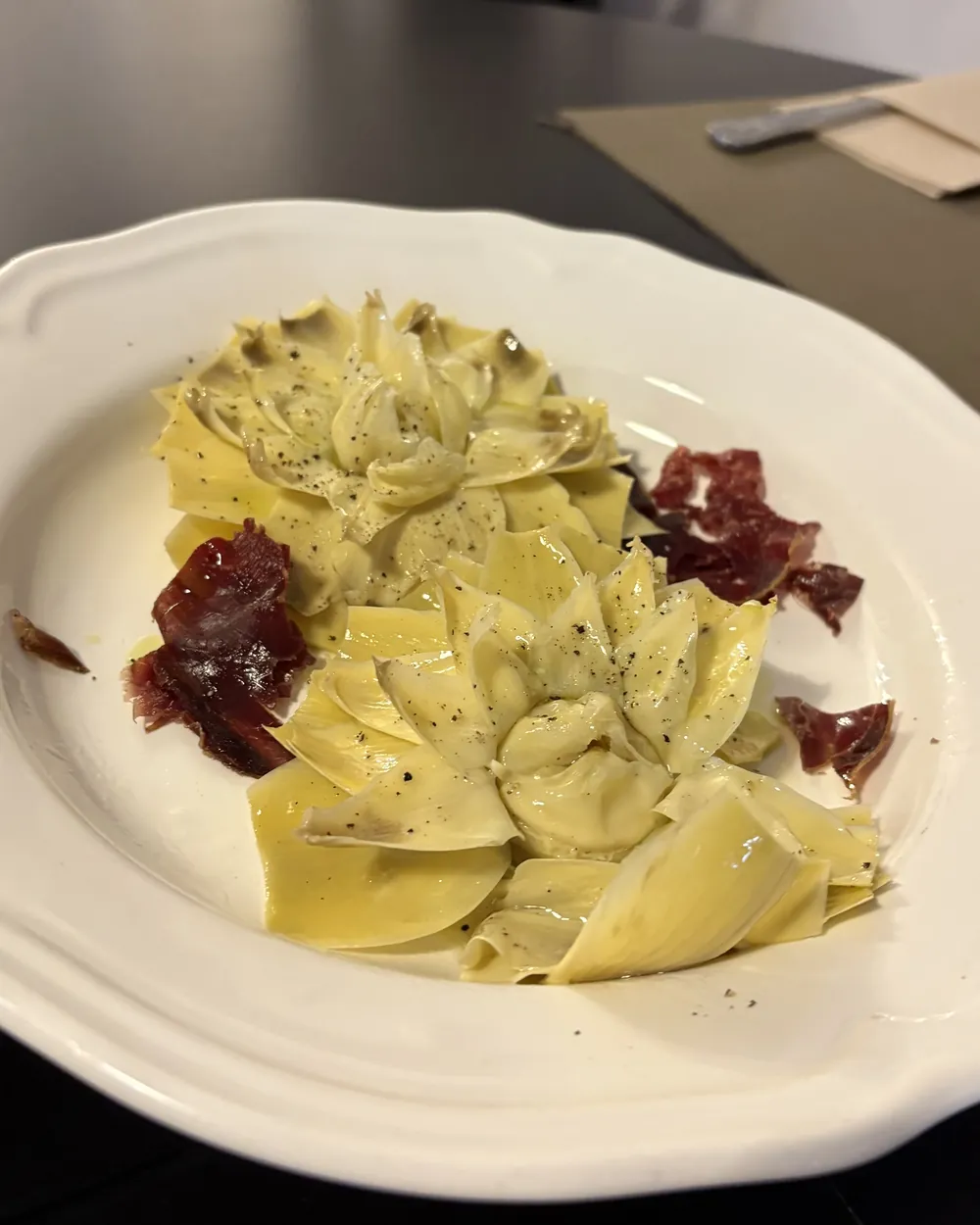 Flor de alcachofa confitada con crujiente de cecina en plato blanco