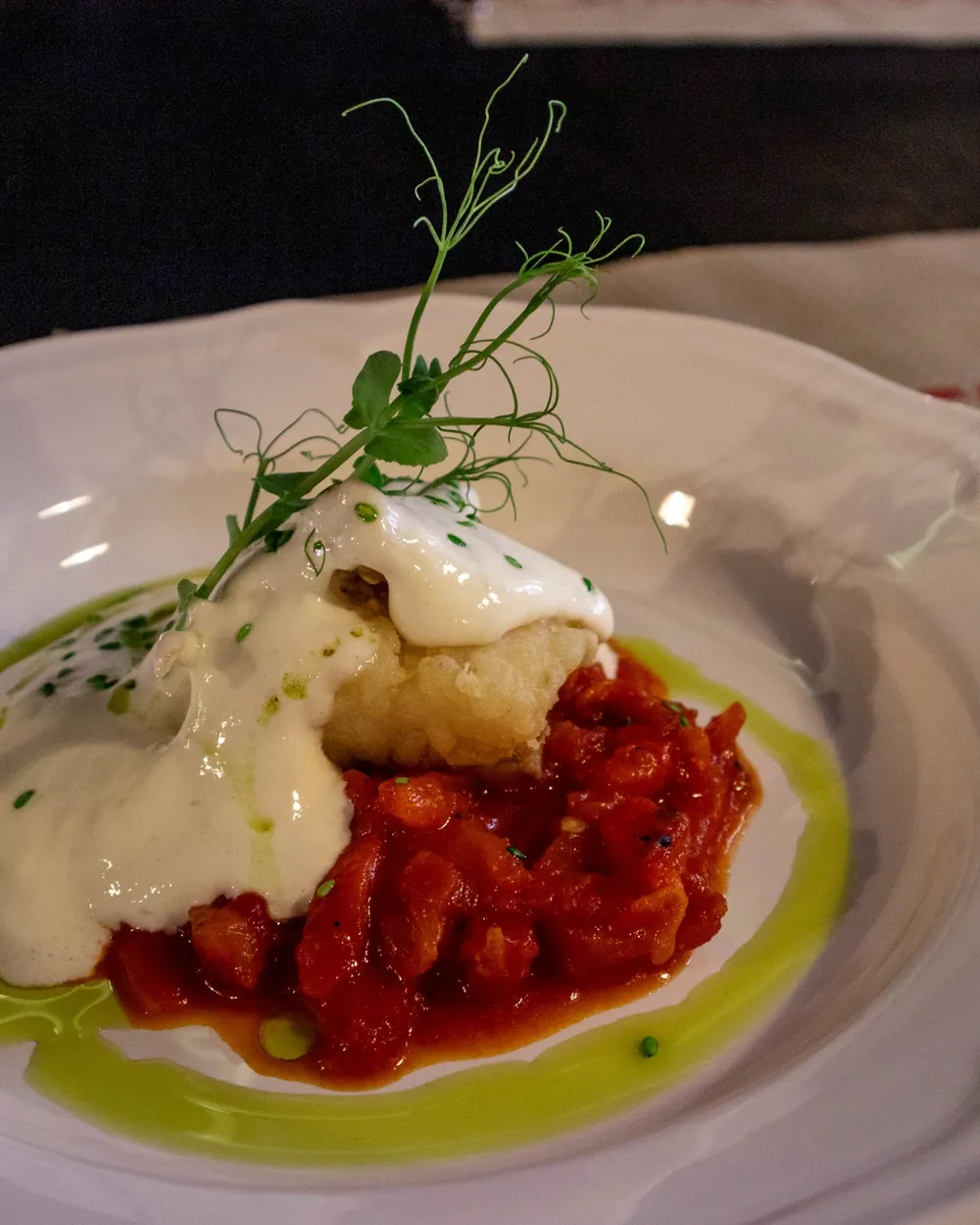 Bacalao con espuma de alioli sobre pimientos asados y aceite verde en plato blanco