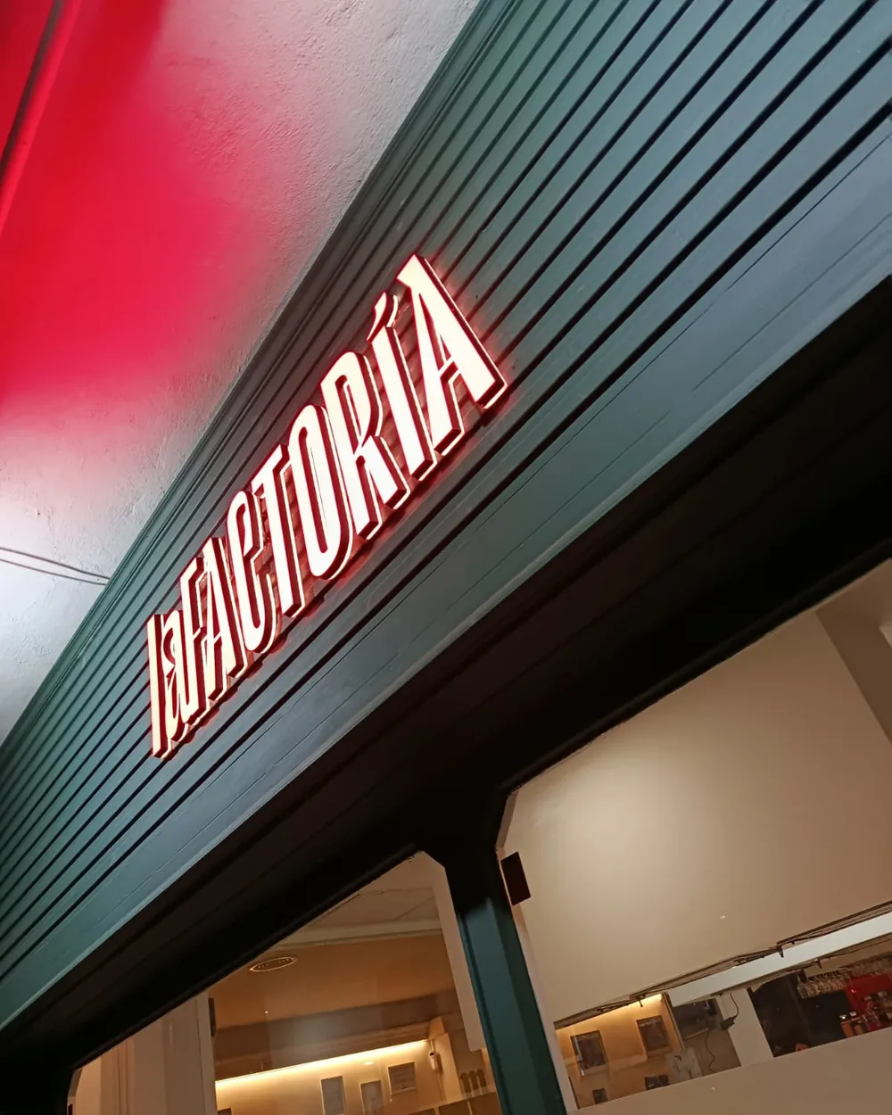 Rótulo luminoso rojo de La Factoría sobre la fachada de lamas verdes
